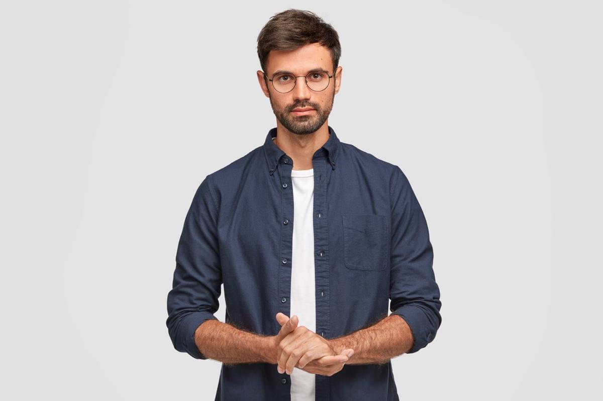 waist-up-portrait-handsome-serious-unshaven-male-keeps-hands-together-dressed-dark-blue-shirt-has-talk-with-interlocutor-stands-against-white-wall-self-confident-man-freelancer.jpg