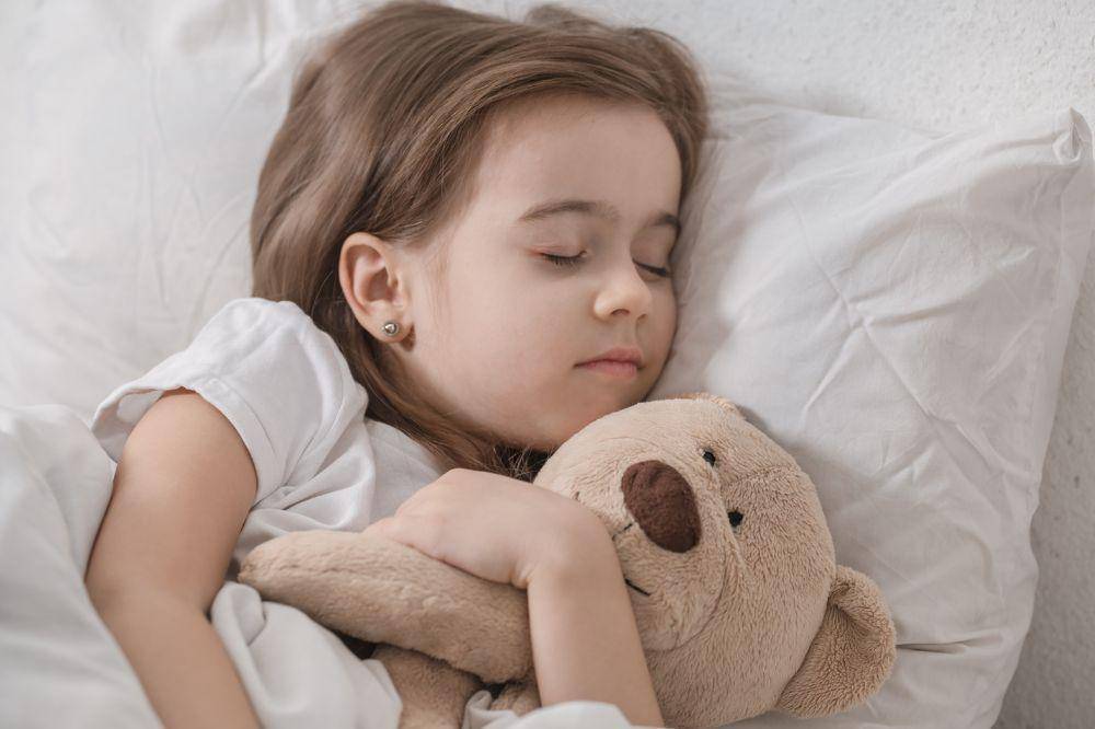 Anak perempuan tidur memeluk boneka