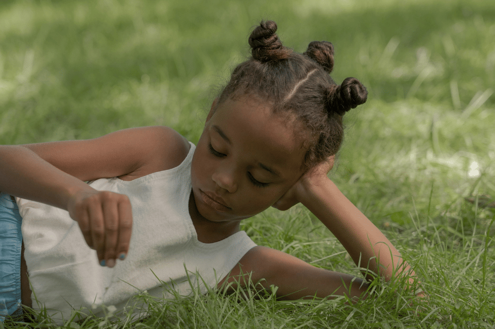Anak berbaring sambil memainkan rumput