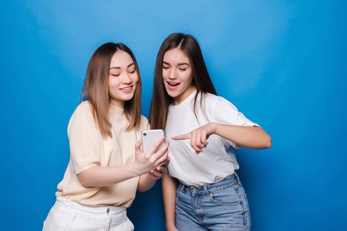 ilustrasi pertemanan dua wanita yang sedang tertawa dan jari telunjuk ke layar smartphone (freepik.com/diana-grytsku)
