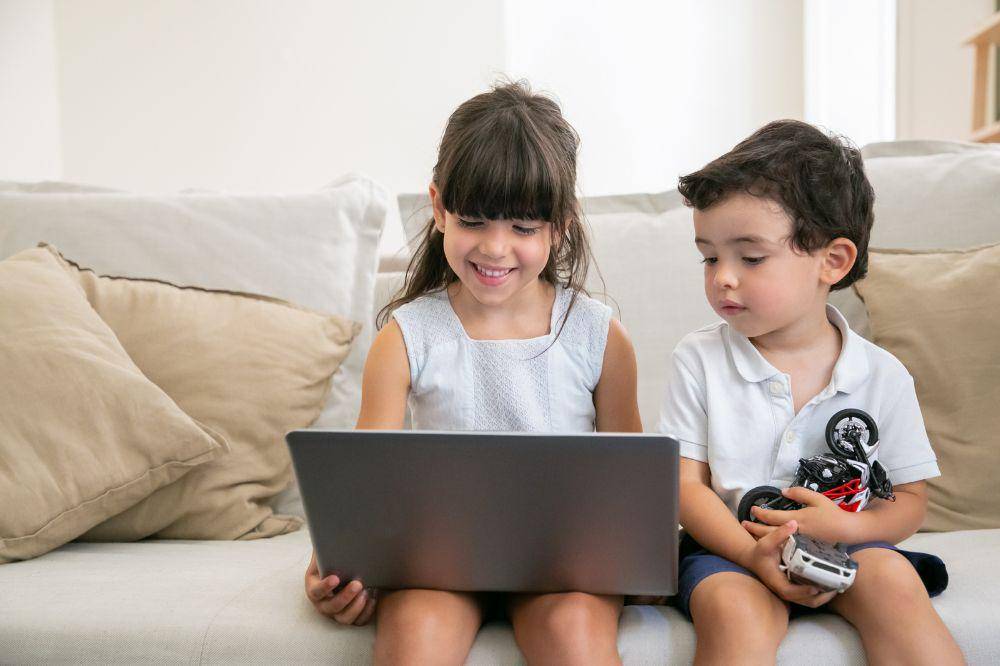 Joyful girl and her little brother using laptop