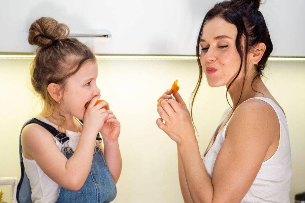 Cute young girl eating orange with mother