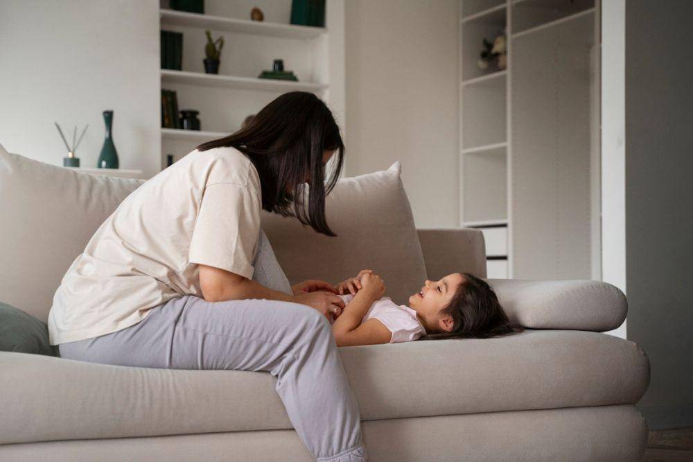Mother tickling kid on couch