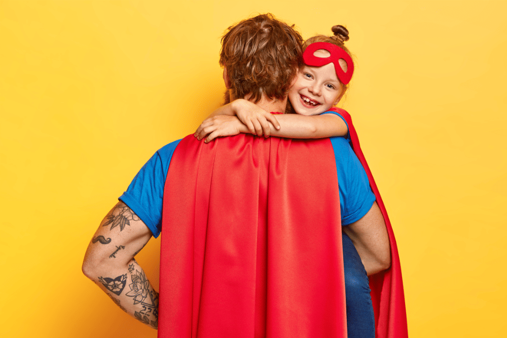 Papa sedang memeluk anak perempuannya dengan menggunakan baju pahlawan