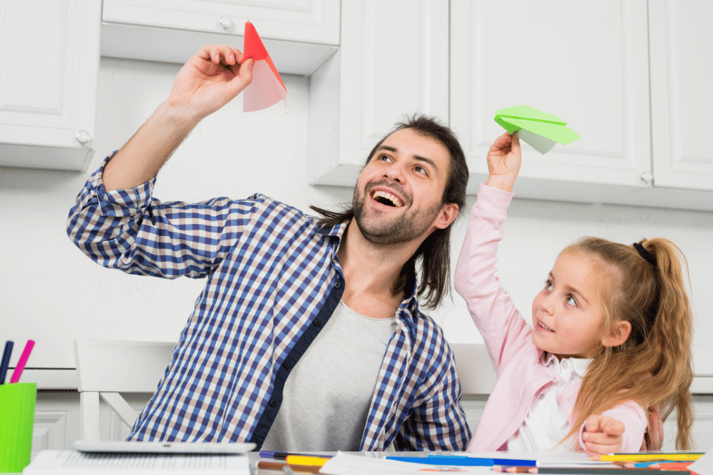 Papa dan anak perempuan sedang bermain pesawat kertas bersama