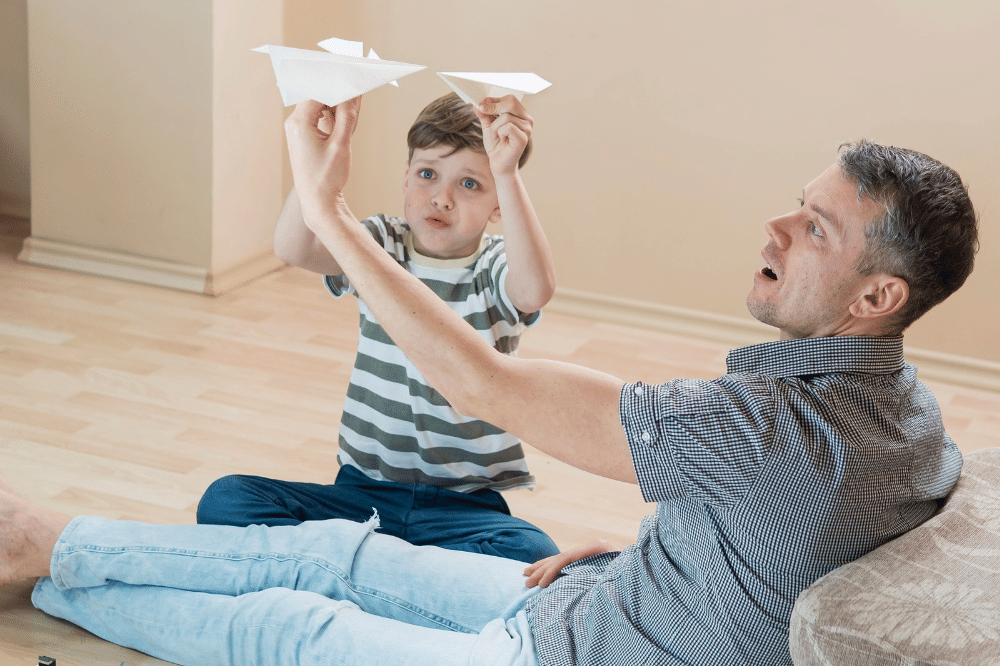 Papa sedang bermain pesawat kertas bersama anak laki-laki