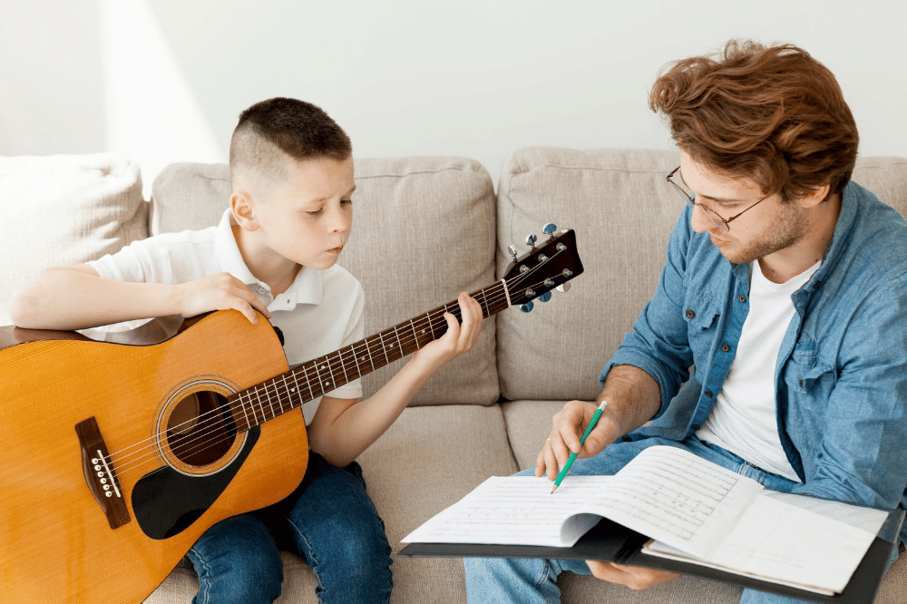 Anak laki-laki sedang belajar main gitar dengan Papa