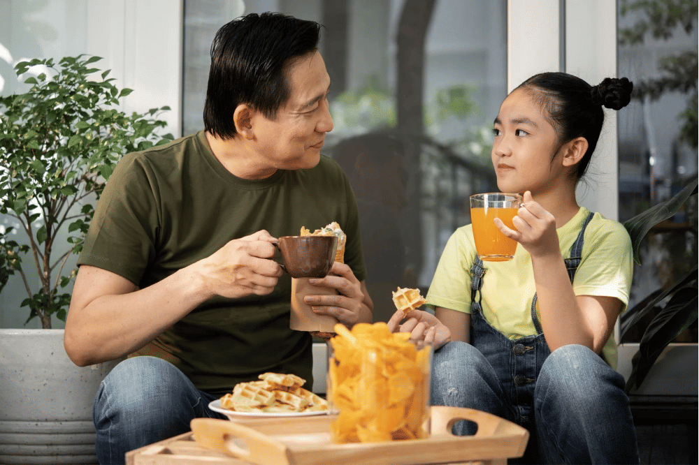 Papa sedang memerhatikan anak perempuannya saat sedang mengobrol sambil mencamil di rumah