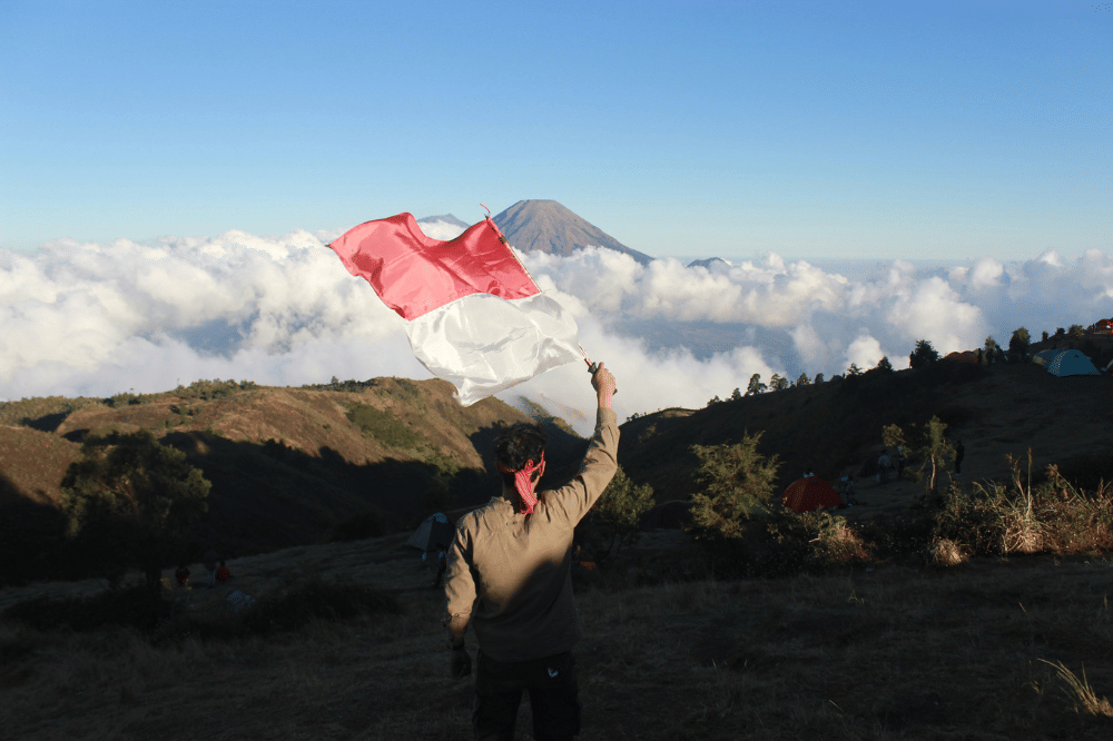 Seseorang memegang bendera merah putih di atas gunung