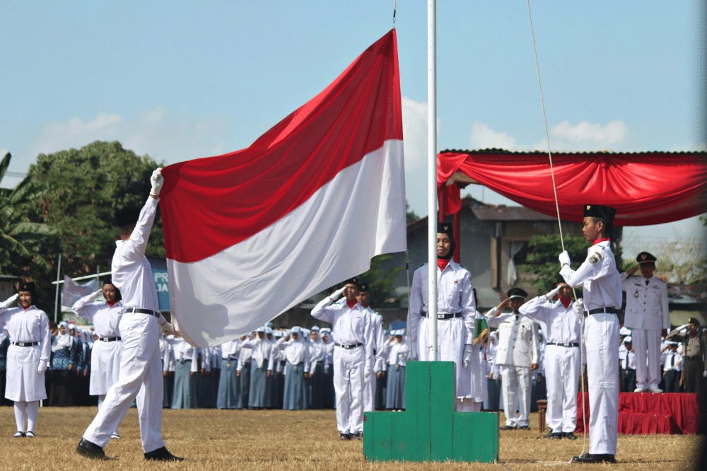 Anak-anak sekolah sedang melakukan upacara dan salah satu anak laki-laki memegang bendera merah putih