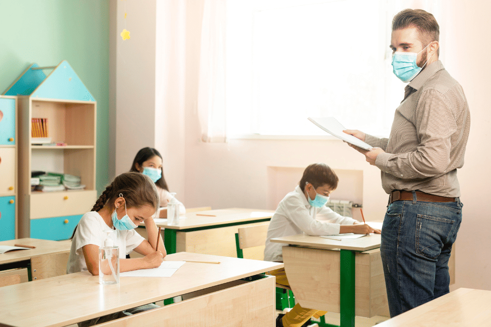 Guru sedang mengajar di kelas dan semuanya terlihat menggunakan masker