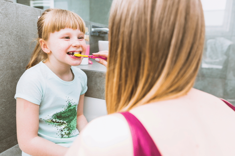 Sorang anak perempuan dibantu Mama untuk menyikat gigi