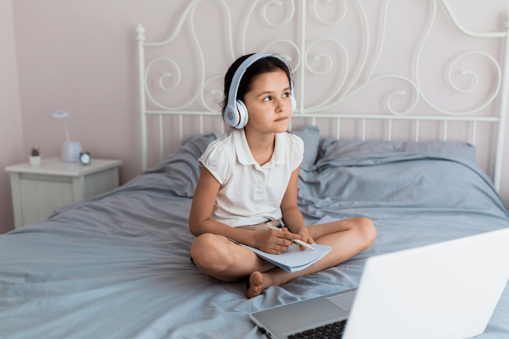 Anak perempuan sedang belajar sambil menggunakan headphone dan laptop
