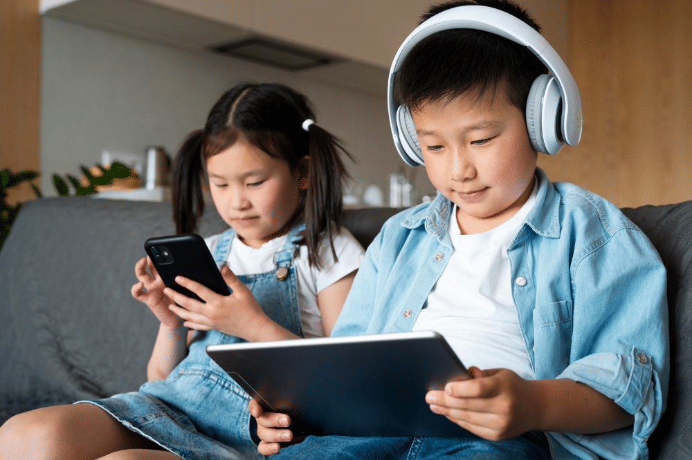 Kedua anak tersebut sedang sibuk dengan gadget masing-masing