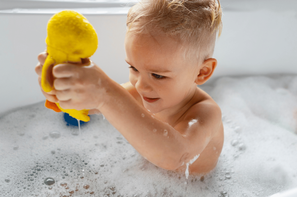 Anak laki-laki sedang mandi dengan busa yang banyak dan mainan
