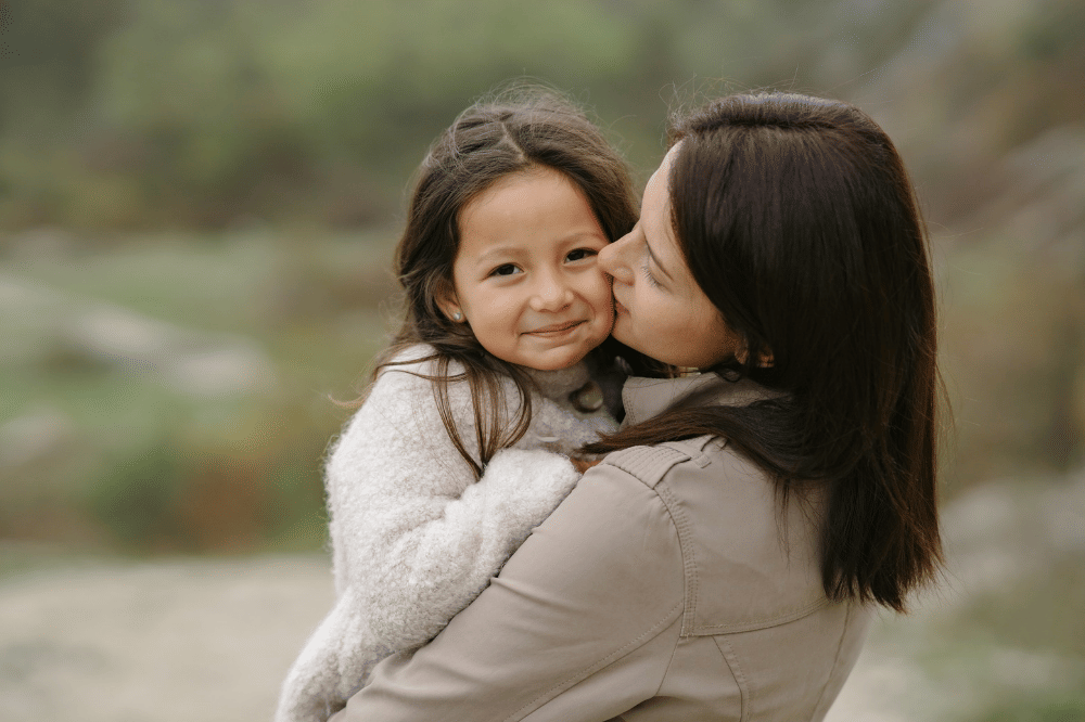Mama menggendong anak perempuan sambil menciumnya