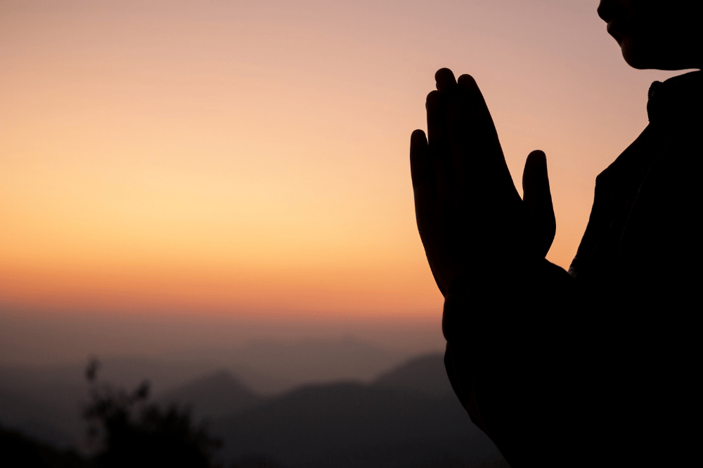 Seseorang sedang memohon kepada Tuhan dengan pemandangan matahari tenggelam yang indah