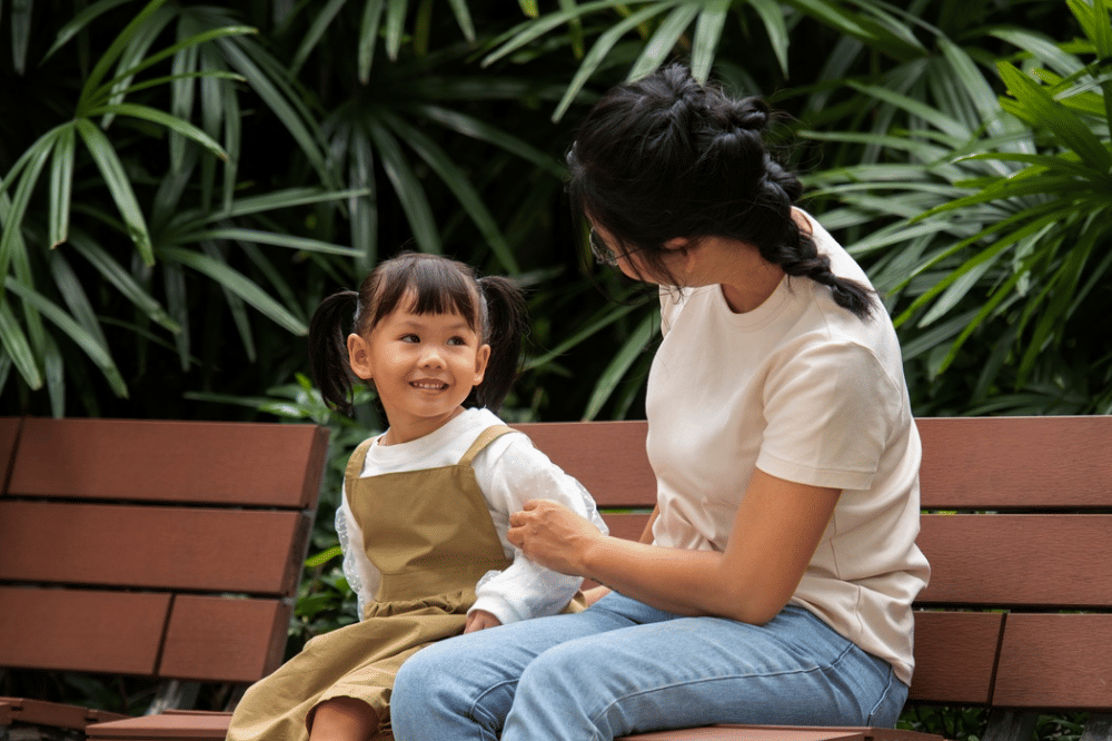 Mama dan anak perempuan sedang duduk bersama di kursi taman