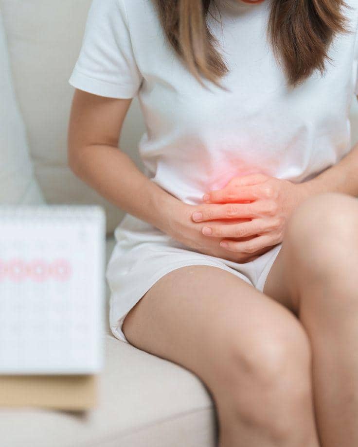 Seorang perempuan duduk sambil memegang perut bagian bawah dengan cahaya merah menandakan rasa nyeri menstruasi.