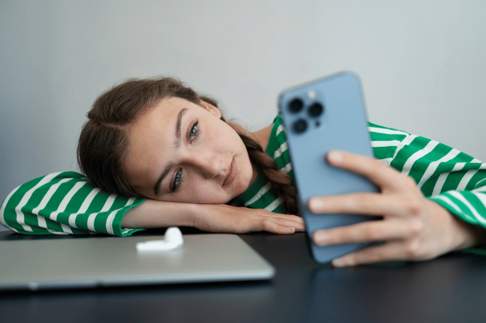 Remaja perempuan sedang menggunakan handphonenya sambil telungkup