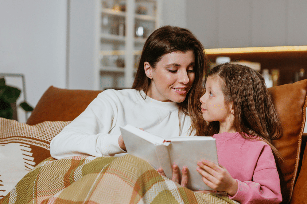 Mama sedang membacakan buku pada anak perempuan sambil berselimut