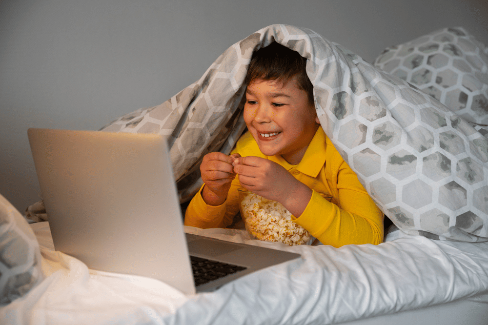 Anak laki-laki menonton film di balik selimut sebelum tidur