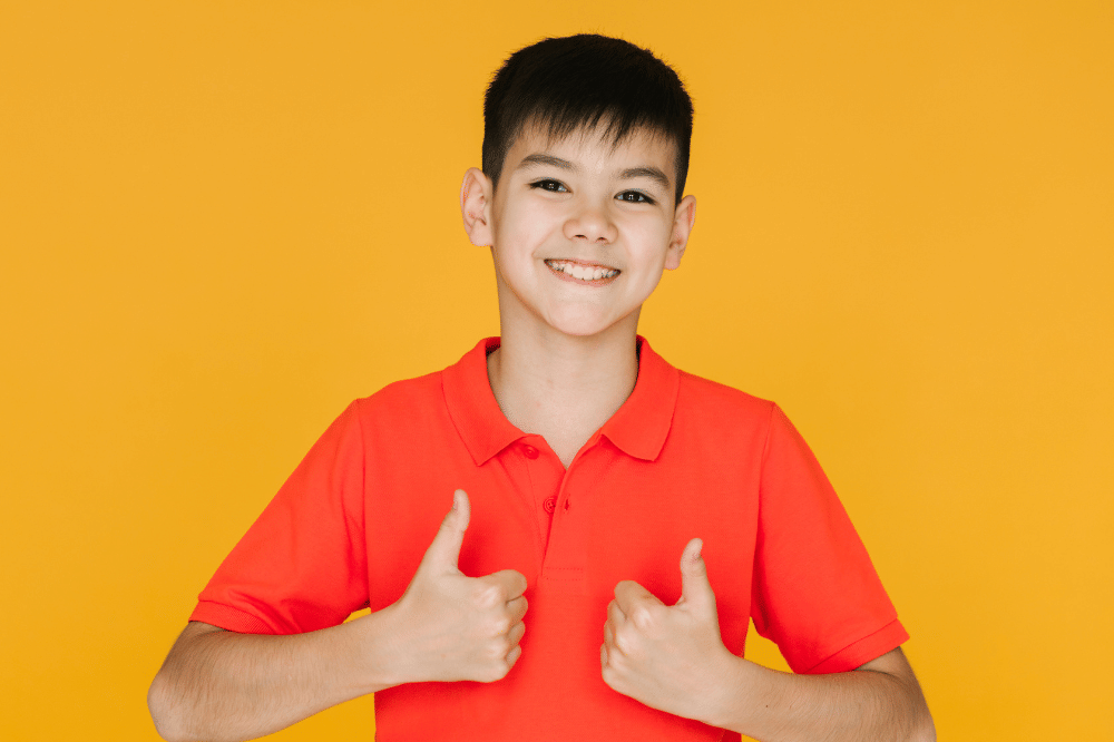 Anak laki-laki mengacungkan dua jempol dan tersenyum