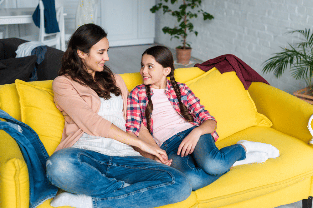 Mama dan anak perempuan sedang berbincang bersama di sofa dengan nyaman