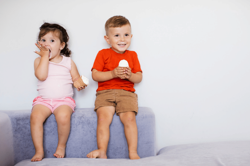Kakak beradik ini sedang makan es krim bersama sambil duduk di sofa