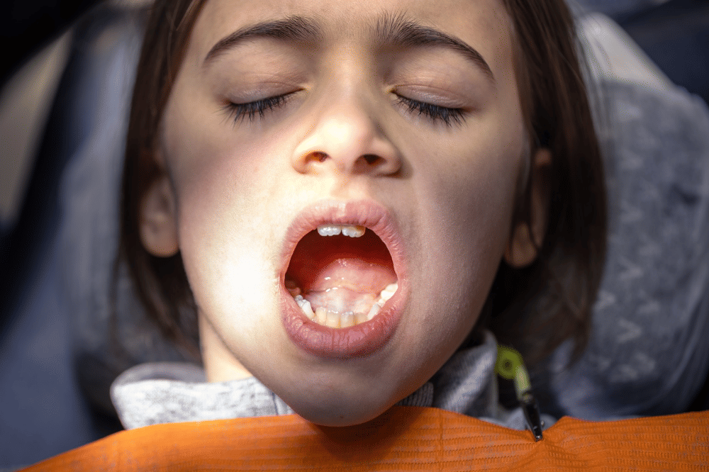 Anak perempuan sedang membuat mulutnya untuk diperiksa oleh dokter