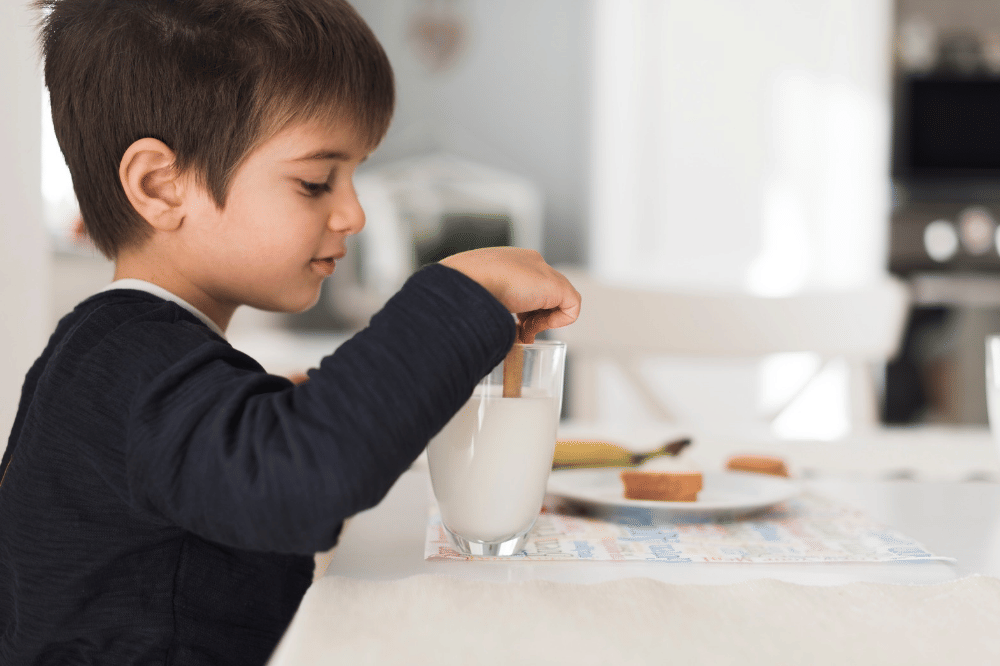 Anak laki-laki sedang mencelupkan biskuit di susu
