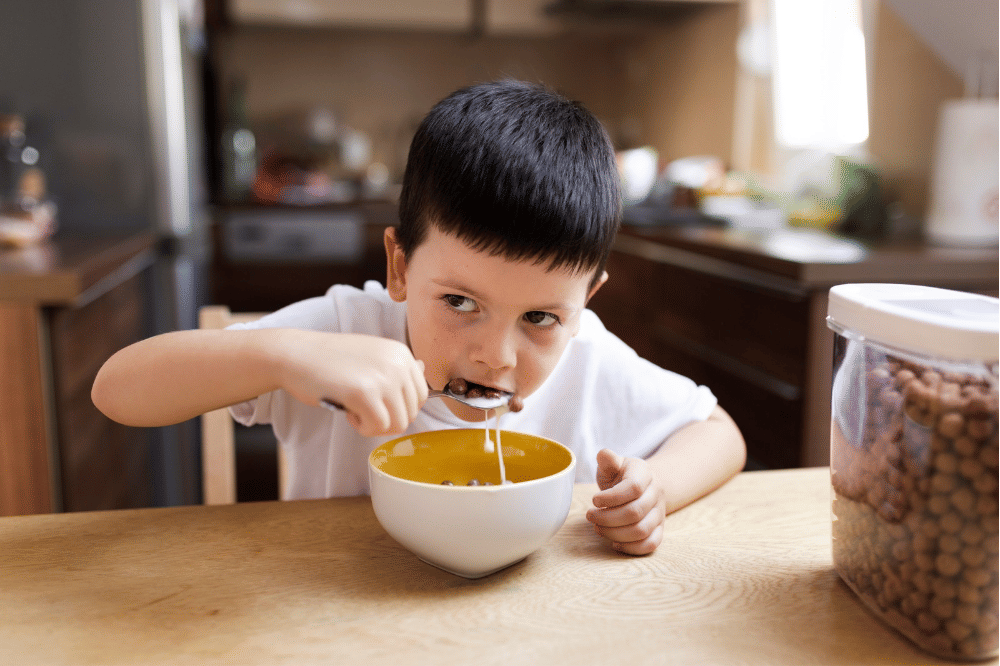 Anak laki-laki sedang makan sereal pakai susu di meja makan