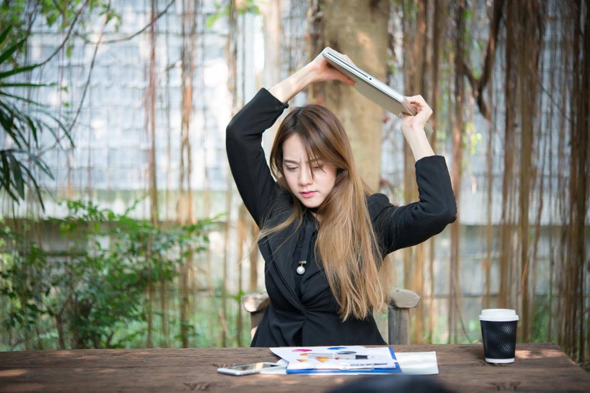 Wanita mengangkat laptop di atas kepala dengan ekspresi emosi