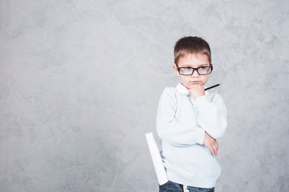 Anak laki-laki berkacamata terlihat serius berpikir sambil memegang pensil