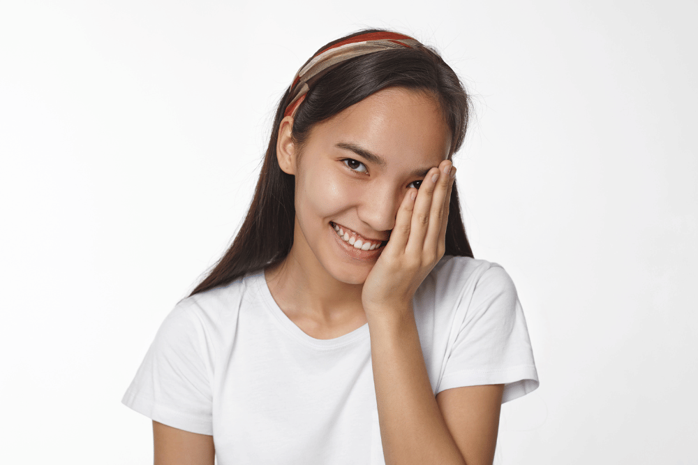 Perempuan sedang dengan kulit sehat itu tersenyum dan menutup sebelah mukanya 