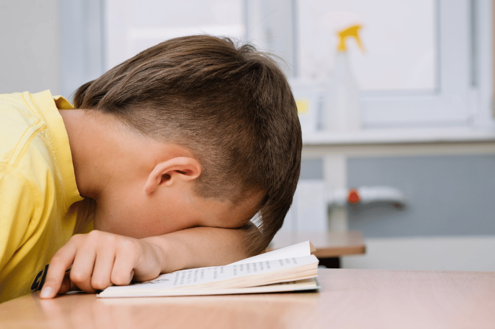 Anak laki-laki menelungkupkan kepalanya diatas tangan dan menimpa buku
