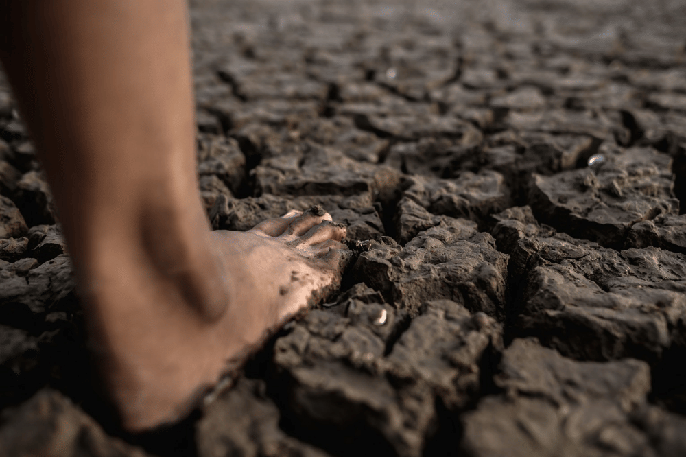 Kaki sedang menginjak tanah yang kering dan gersang di musim kemarau