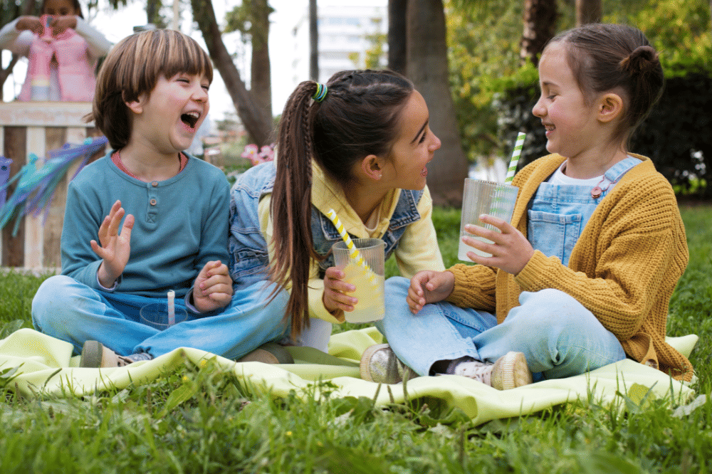 Anak-anak tersebut sedang mengobrol dan bercanda sambil duduk di taman dan minum lemonade