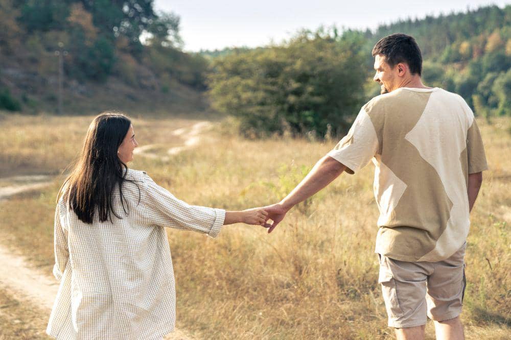 A man and a woman walk into a field holding hands