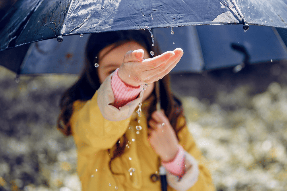 Anak perempuan memakai payung dan menadah hujan dengan tangannya