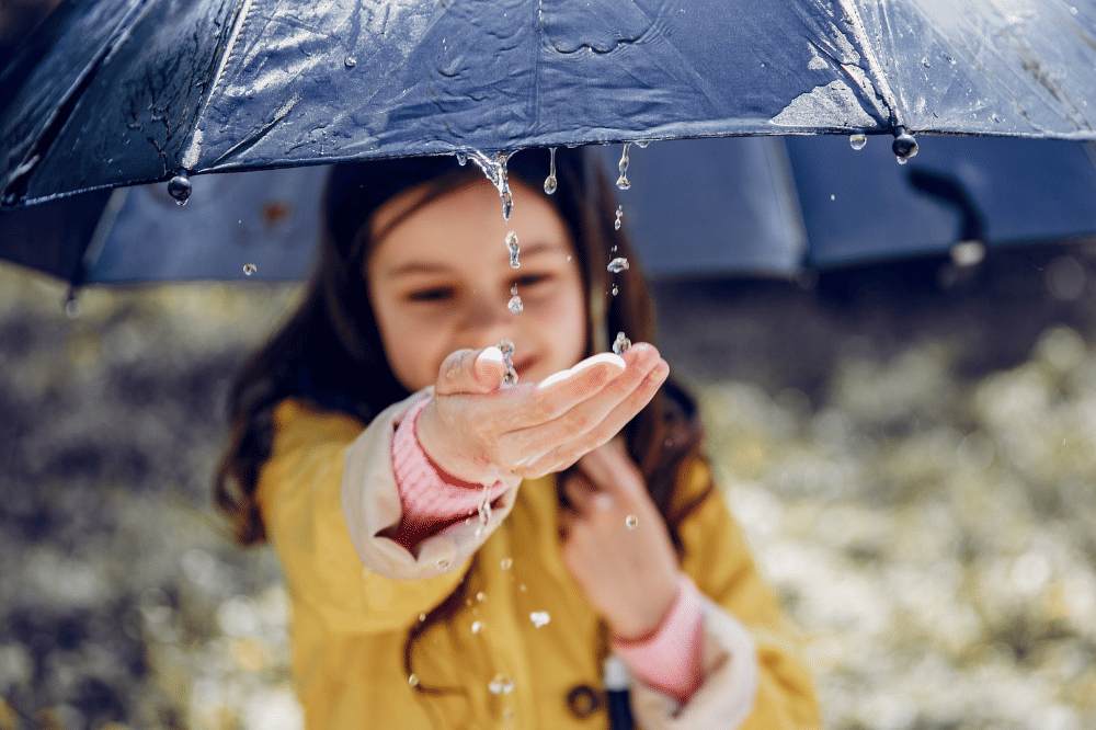Anak perempuan memakai payung dan menadah hujan dengan tangannya