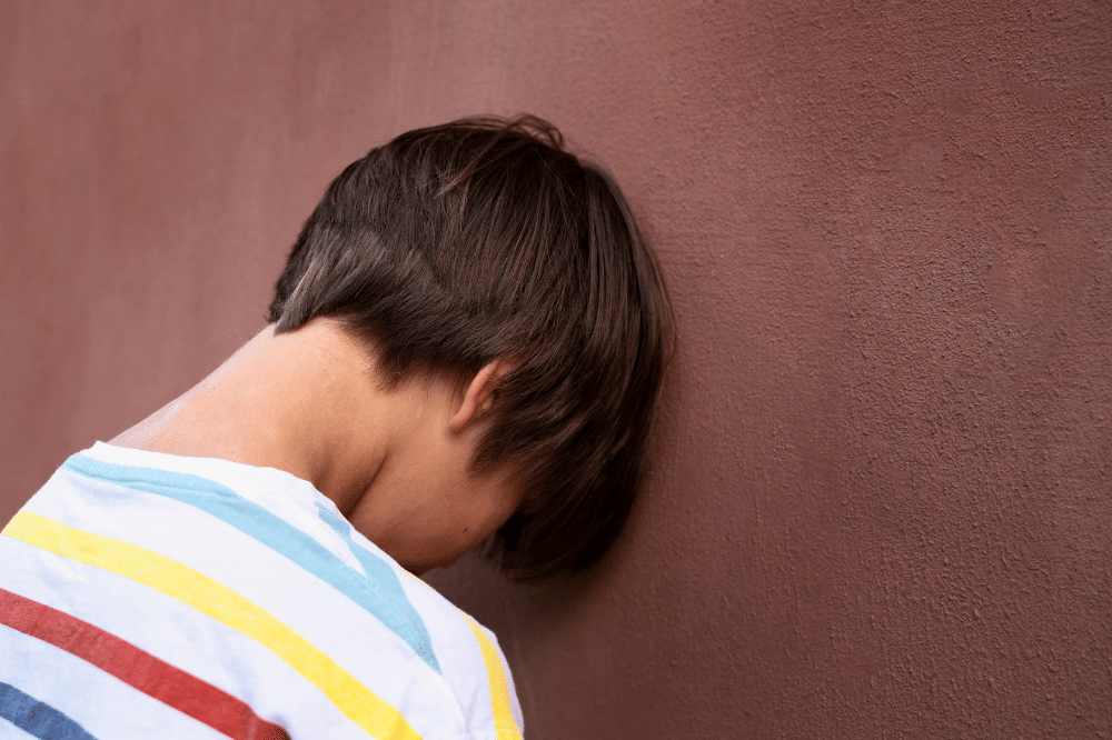 Anak laki-laki menempelkan kepanya pada dinding dan terlihat sedih