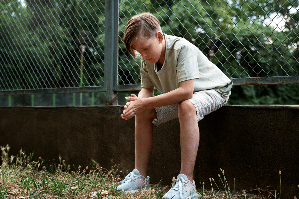 Anak laki-laki duduk dan menangkupkan tangan melihat tanah