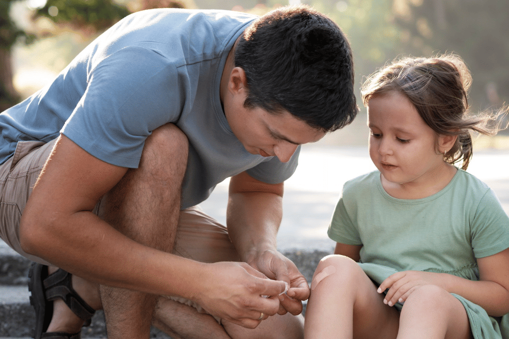 Papa mengajarkan anak cara mengatasi luka kecil di kaki anak perempuannya