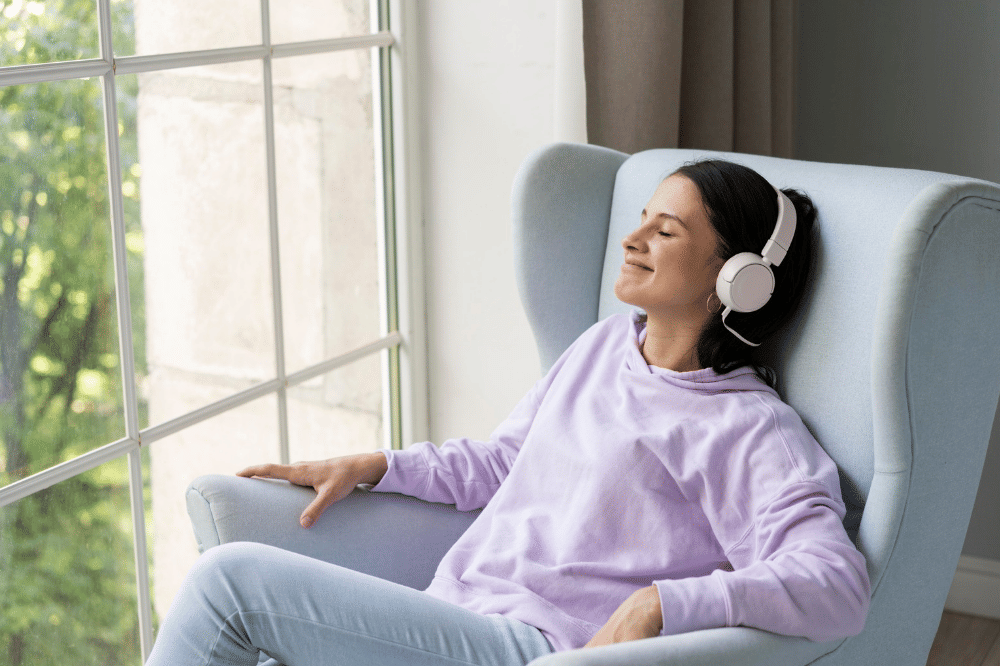 seorang perempuan duduk di sofa sambil memakai headphone untuk bersantai