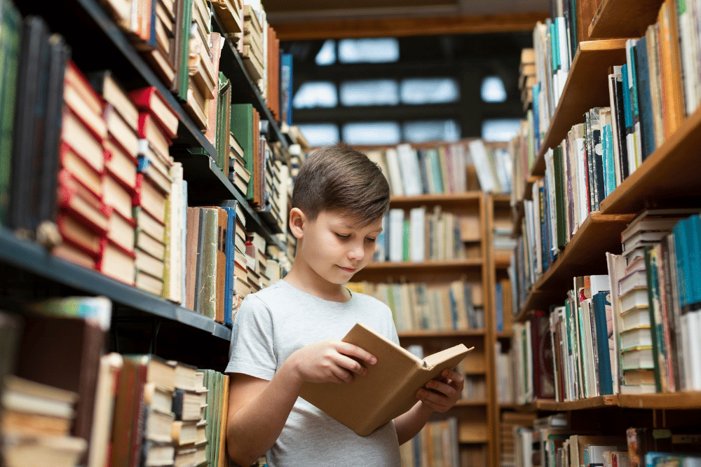 Anak laki-laki sedang membaca buku di perpustakaan