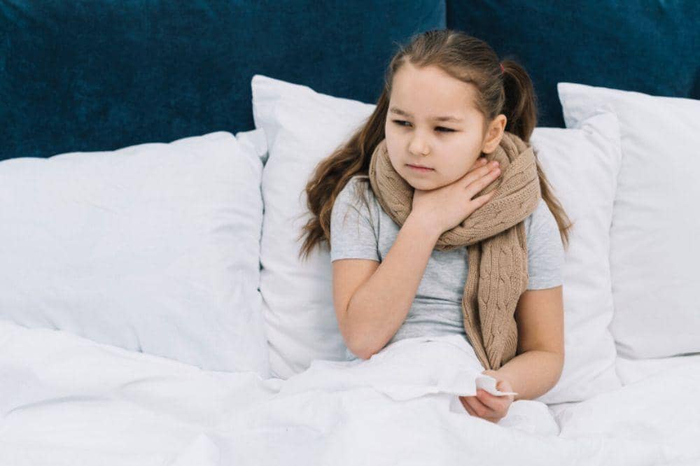 Sick girl sitting on bed with scarf around her neck suffering from sore neck