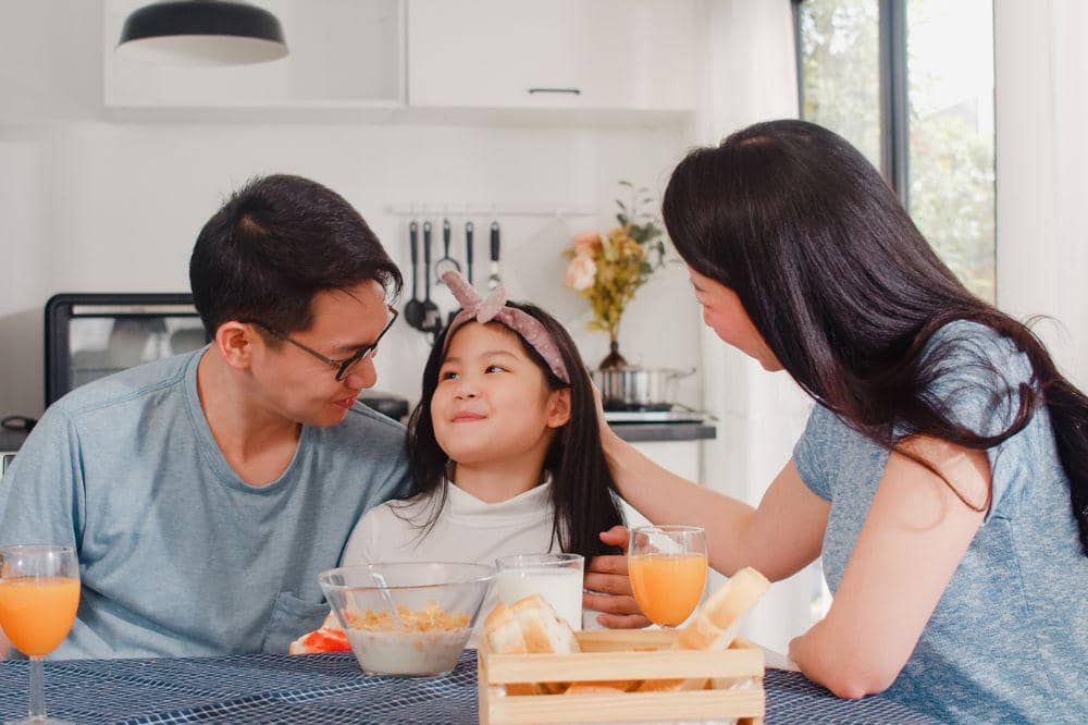 Asian japanese family has breakfast at home. Asian mom, dad, and daughter feeling happy talking together while eat bread, corn flakes cereal and milk in bowl on table in the kitchen in the morning.jpg