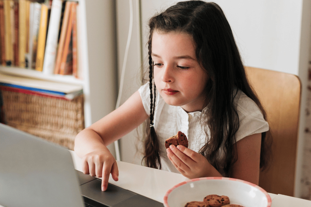 Anak perempuan sedang makan sambil menonton di laptop
