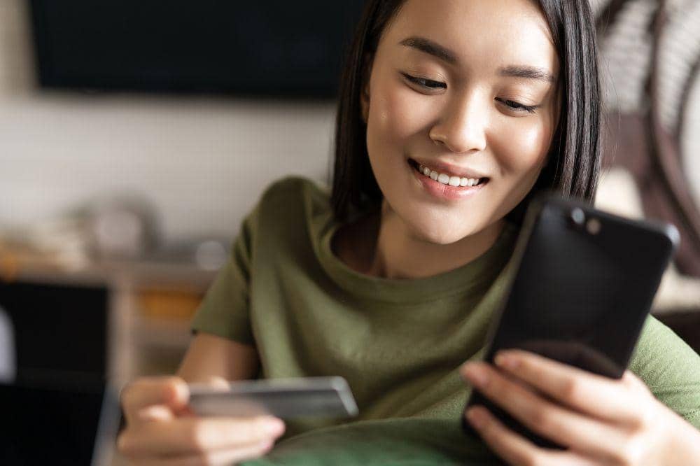 Wanita memegang ponsel dan kartu debit